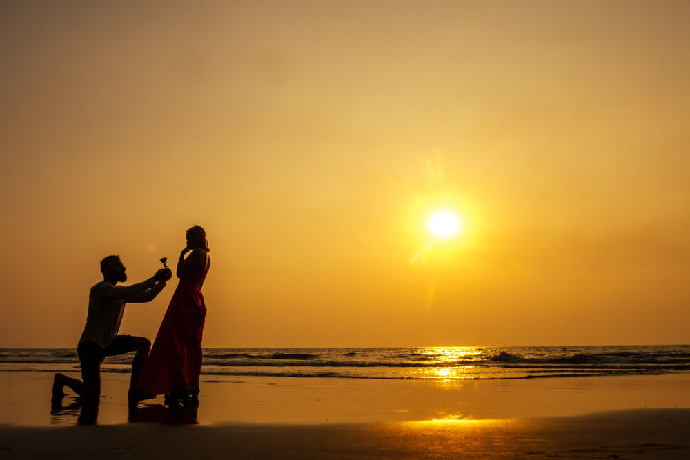 A man and woman during a sunset beach proposal
